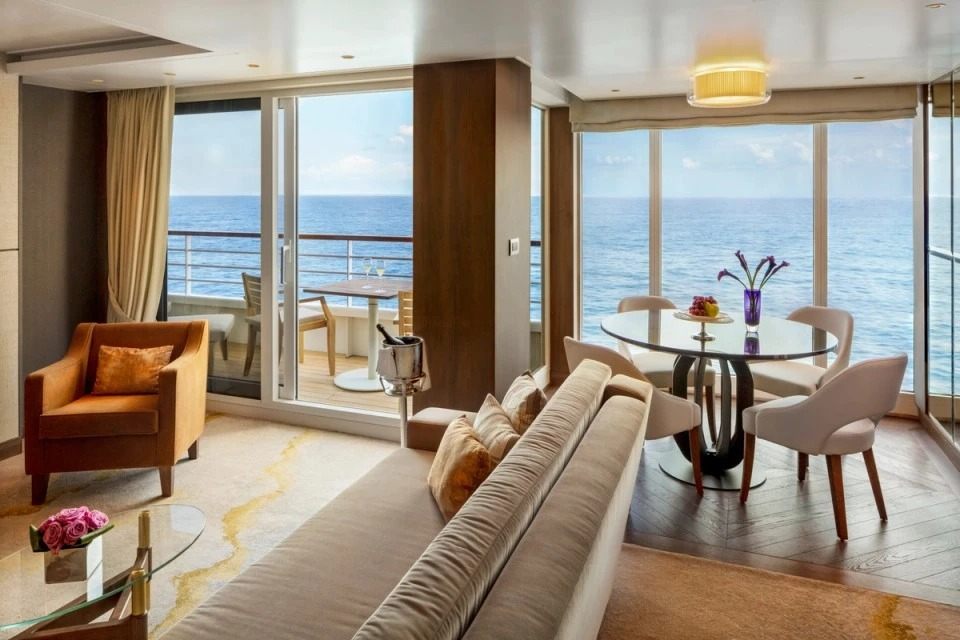 A luxury cruise suite lounge and dining table with floor-to-ceiling ocean-view windows